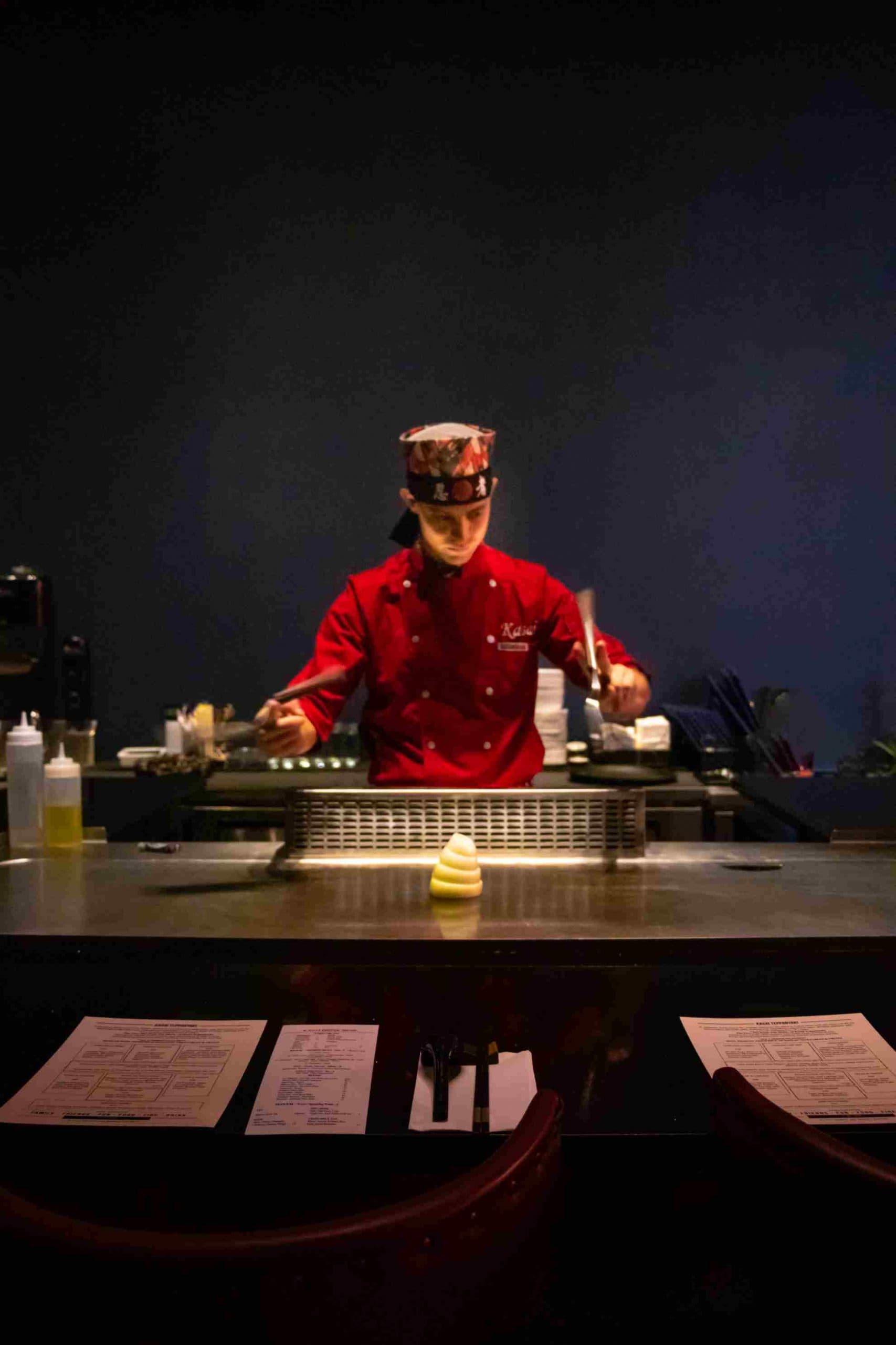 A chef in Kasai red preparing the grill under a spotlight