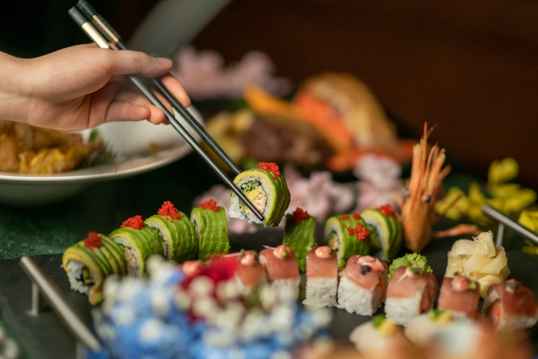 Chopsticks lifting a roll from a colourful platter of specialty sushi