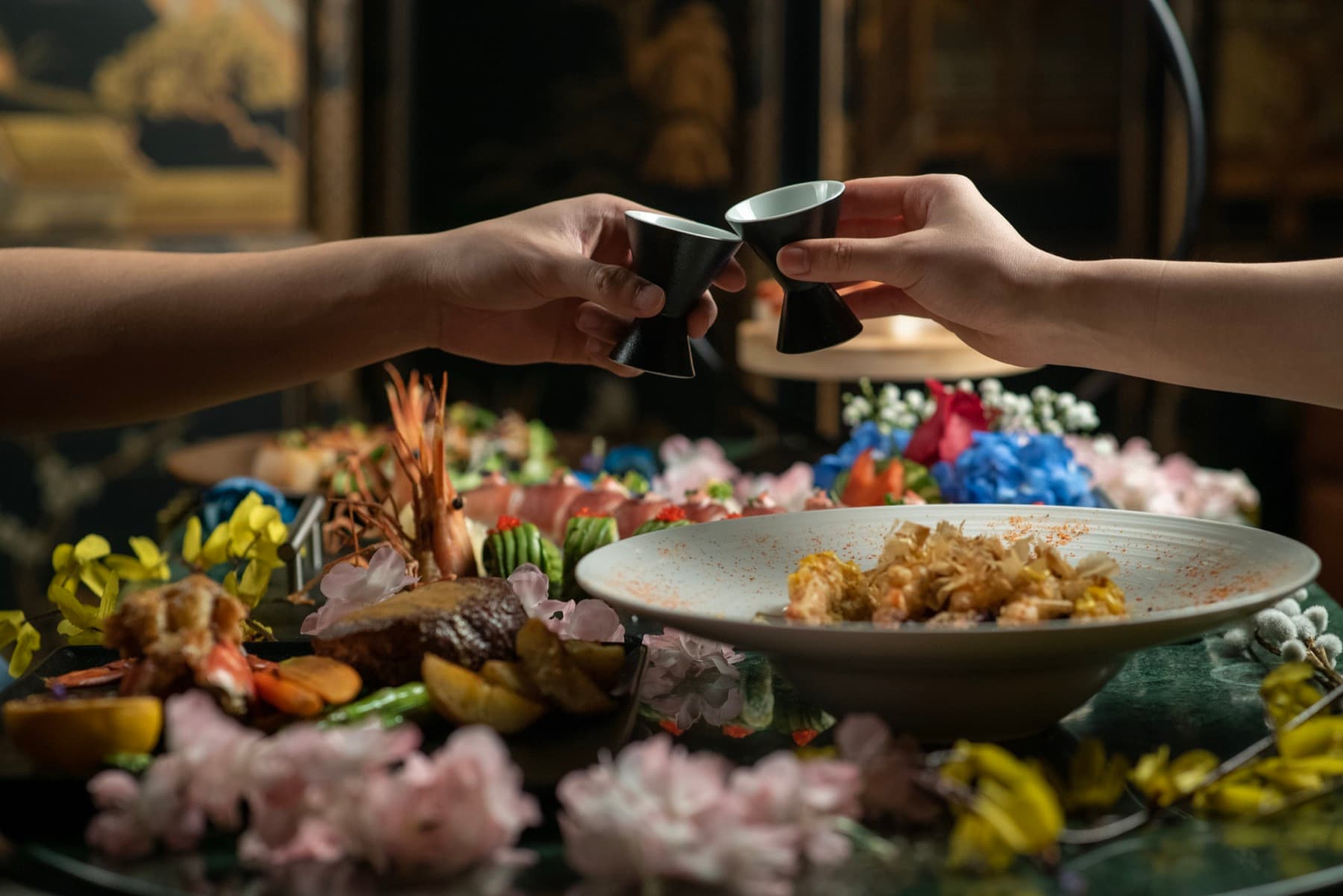 Two guests toasting with sake cups over a seafood platter